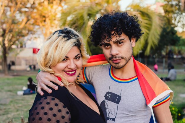 L'uomo omosessuale con la bandiera dell'orgoglio abbraccia la sua amica all'aperto guardando la fotocamera