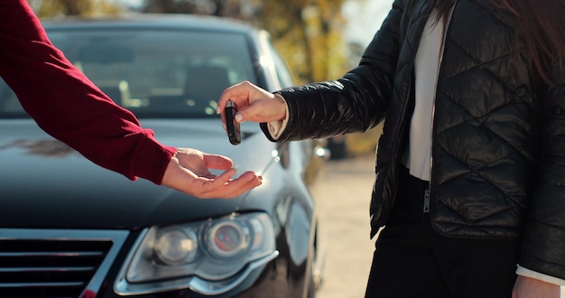 L'uomo ottiene la chiave dell'auto dal venditore - soddisfatto - commercio chiuso - nuova auto in background. Concetto di acquisto di un veicolo, affari automobilistici.