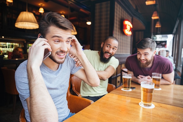 L'uomo parla al telefono mentre gli amici divertenti i suoi amici non gli permettono di farlo nel pub della birra