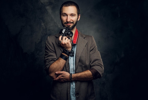 L'uomo pensieroso attraente con la macchina fotografica sta posando per il fotografo nello studio fotografico scuro.