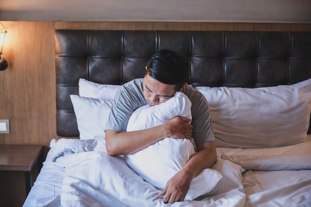 L'uomo pigro dorme mentre è seduto e abbraccia un cuscino su un letto