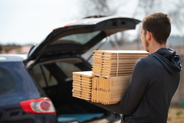 L'uomo porta il parquet all'auto Materiali da costruzione per la riparazione e la decorazione dei locali Materiale in legno