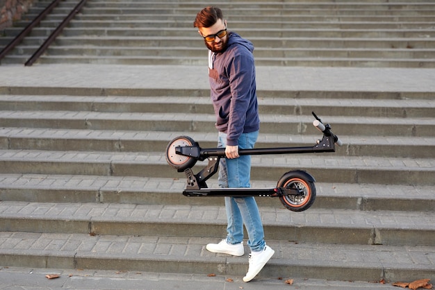 L'uomo porta lo scooter elettrico in posizione ripiegata Ragazzo che trasporta lo scooter elettrico piegato in mano sulle scale L'uomo indossa abiti eleganti e tiene lo scooter elettrico