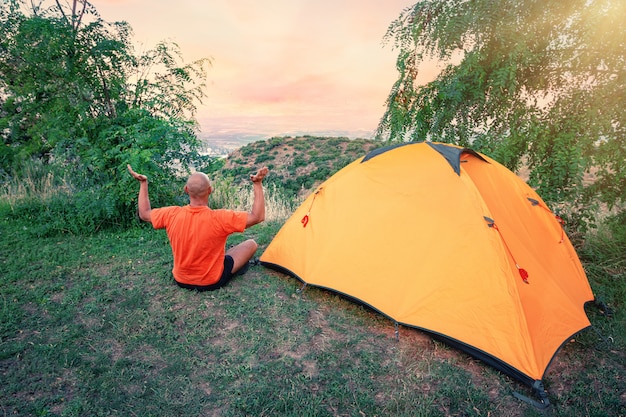 L'uomo pratica yoga vicino a una tenda arancione sulla collina