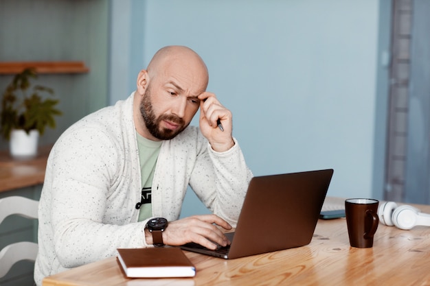 L'uomo premuroso sta scrivendo su un computer portatile, lavora a casa, lavora online, coronavirus