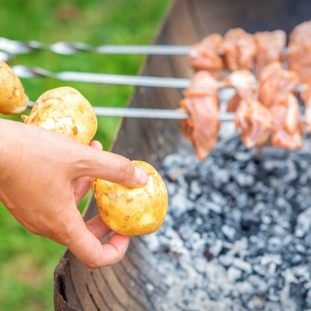 L'uomo prepara la carne al barbecue con le patate