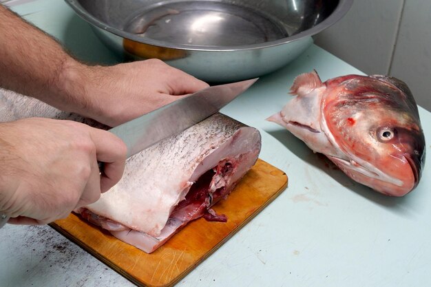 L'uomo prepara pesce carpa d'argento fresco e lo taglia in bistecche con un coltello.