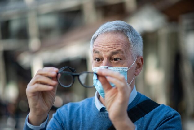 L'uomo pulisce gli occhiali appannati a causa del concetto di visione del coronavirus covid della maschera