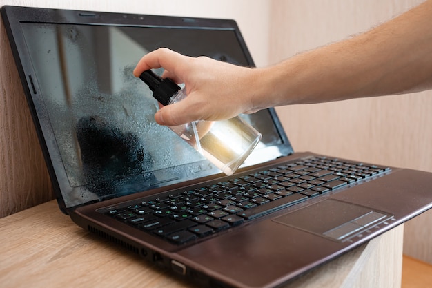 L'uomo pulisce il laptop con uno spray alcolico