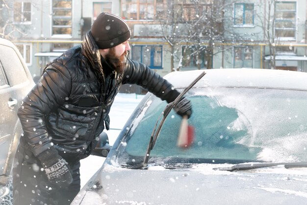 L'uomo pulisce la neve dal vetro dell'auto