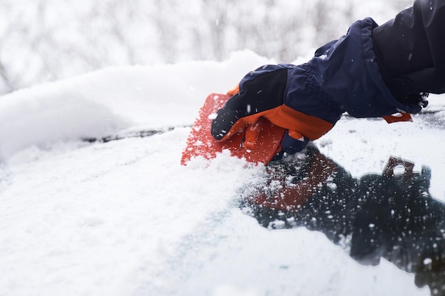 L'uomo pulisce la sua auto dopo una nevicata Pulizia della neve dal parabrezza Raschiatura del ghiaccio Pulizia dei vetri dell'auto invernale