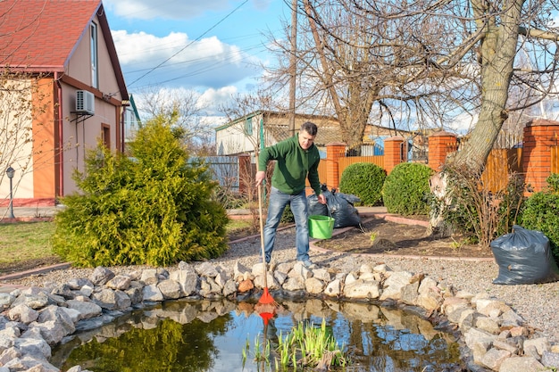L'uomo pulisce un laghetto da giardino da piante acquatiche e foglie che cadono