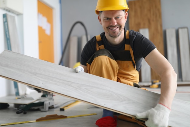 L'uomo qualificato del falegname porta la tavola di legno sul lavoratore energico del progetto di lavoro