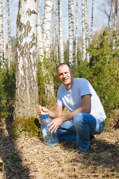 L'uomo raccoglie la linfa di betulla nella foresta di primavera