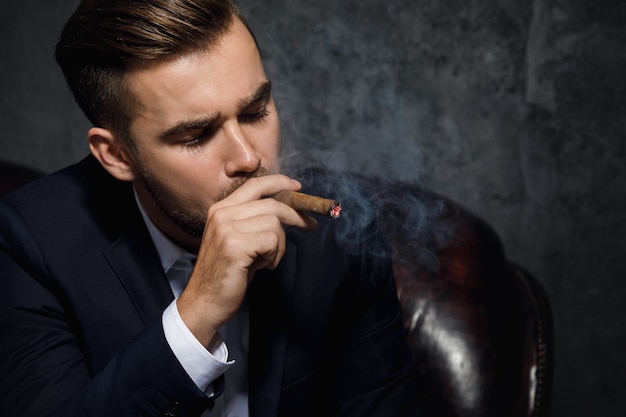 L'uomo ricco bello sta fumando il sigaro