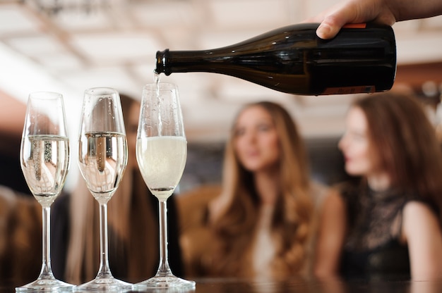 L'uomo riempie bicchieri di champagne per tre belle giovani donne