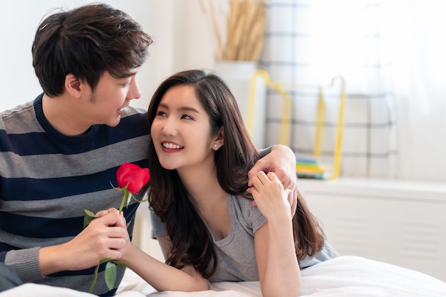 L'uomo romantico che dà una rosa alla bella donna, bella coppia asiatica elegante sta abbracciando e sorridendo nella camera da letto.