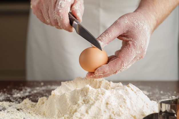 L'uomo rompe l'uovo sopra la farina bianca per fare un impasto per ravioli o gnocchi