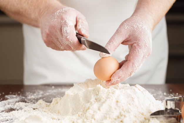 L'uomo rompe l'uovo sopra la farina bianca per fare un impasto per ravioli o gnocchi