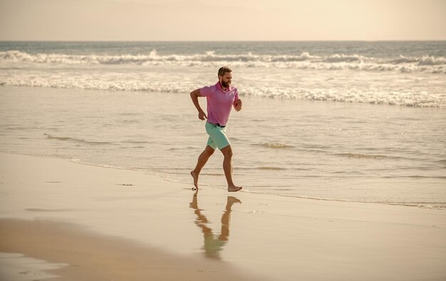 L'uomo sano che corre sulla spiaggia energico corridore estivo sente la libertà godendosi la mattina