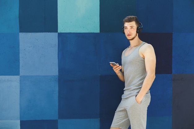 L'uomo sceglie la musica da ascoltare nel suo telefono cellulare durante il jogging in città, copia spazio, sfondo blu brillante