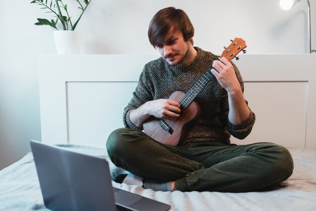 L'uomo seduto a casa impara a suonare le ukulele usando le lezioni online.