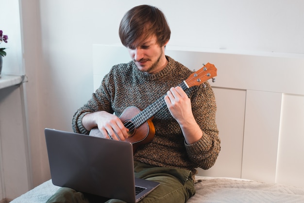 L'uomo seduto a casa impara a suonare le ukulele usando le lezioni online.