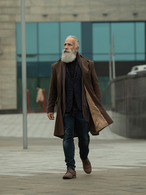 L'uomo senior alla moda con barba e capelli grigi è all'aperto sulla strada.