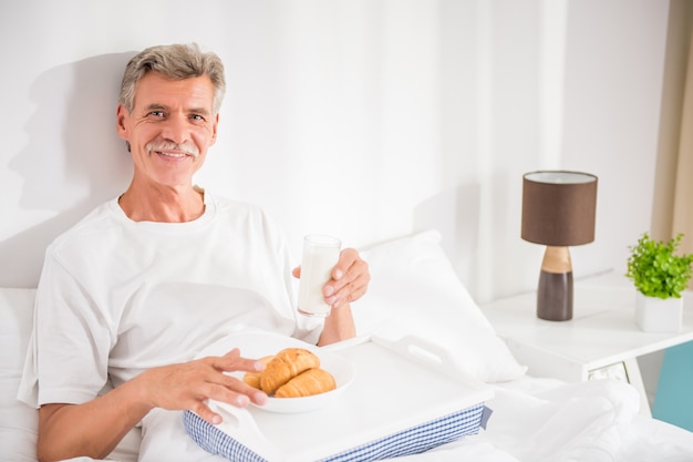L'uomo senior felice sta facendo colazione a letto.