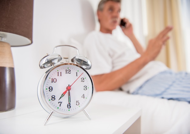 L'uomo senior sta sedendosi nel letto e sta parlando al telefono.