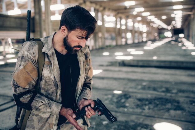 L'uomo serio è in piedi nel capannone e tiene in mano la pistola di paintball.