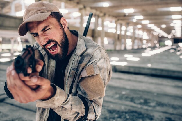 L'uomo serio è in piedi nel capannone e tiene in mano la pistola di paintball.