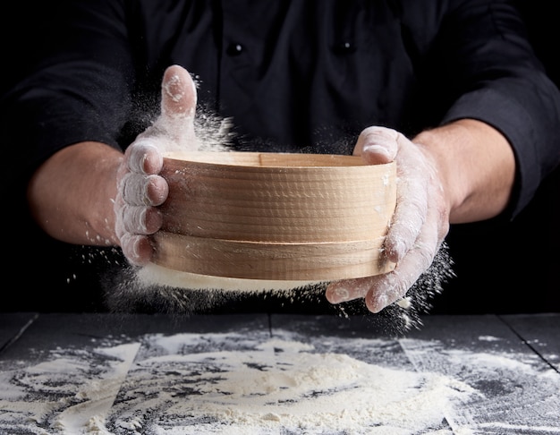 L&#39;uomo setaccia la farina di grano bianco attraverso un setaccio di legno