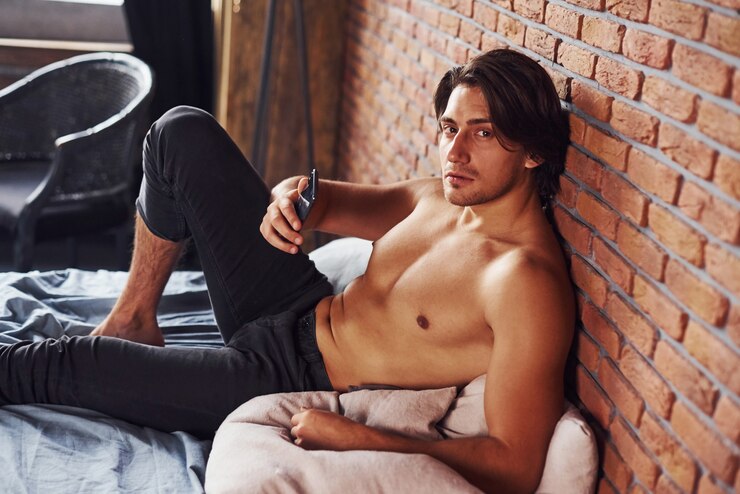 Foto l'uomo sexy a torso nudo riposa da solo nella sua camera da letto al mattino.
