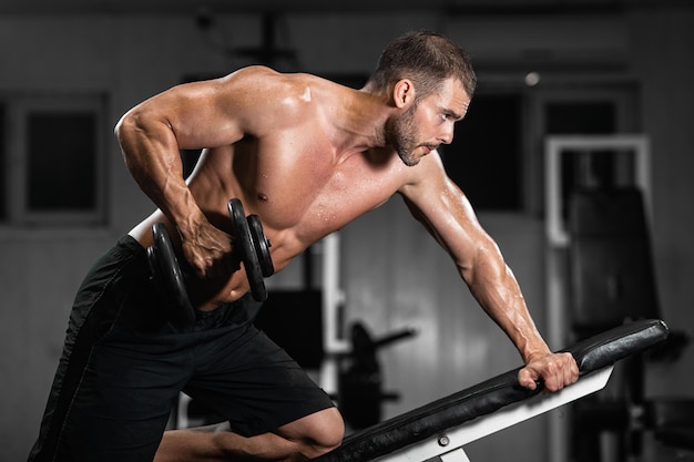 L'uomo si allena in palestra. L'uomo atletico si allena con le teste di legno, pompando il suo bicipite