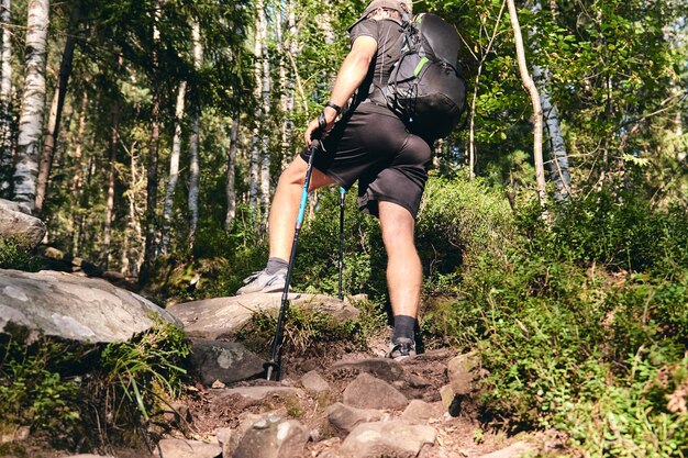 L'uomo si arrampica in scarpe da ginnastica in azione all'aperto. Vista dall'alto dell'escursionismo Boot sul sentiero. Gambe ravvicinate in jeans e scarpe da trekking sportive su pietre rocciose della foresta di montagna.