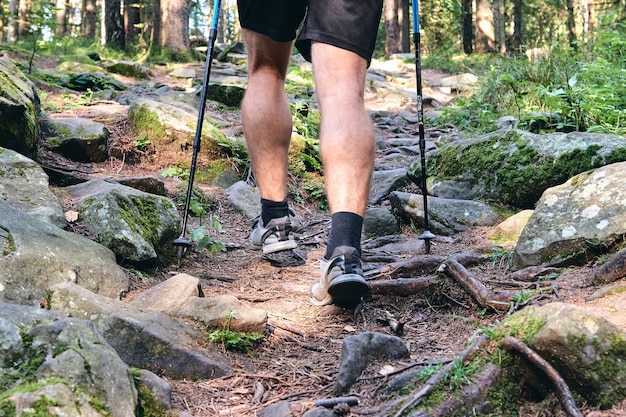 L'uomo si arrampica in scarpe da ginnastica in azione all'aperto. Vista dall'alto dell'escursionismo Boot sul sentiero. Gambe ravvicinate in jeans e scarpe da trekking sportive su pietre rocciose della foresta di montagna.