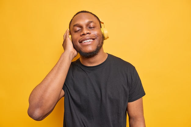 l'uomo si diverte ad ascoltare la musica preferita indossa le cuffie wireless sulle orecchie cattura ogni pezzo di canzone vestito con una maglietta nera isolata su un giallo vivido