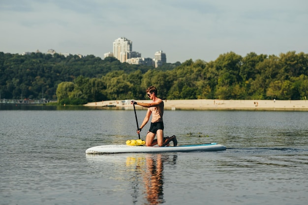 l'uomo si inginocchia su una tavola da sup e nuota sul fiume sullo sfondo di un bellissimo paesaggio