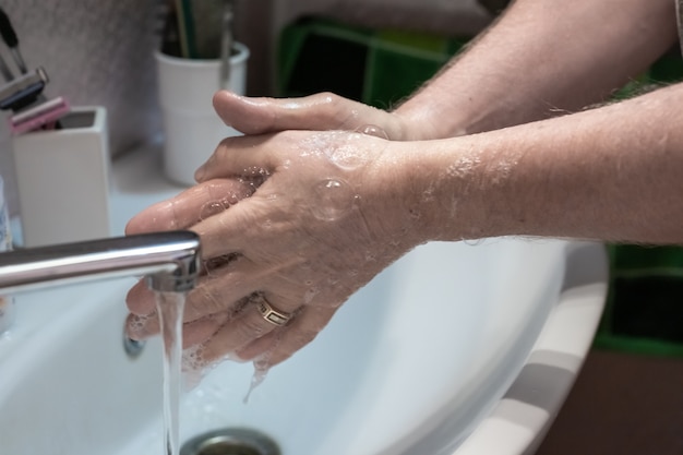 L'uomo si lava le mani con sapone liquido su un lavandino a casa da vicino