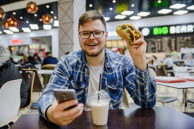 L'uomo si siede al bar mangia hamburger e guarda nel cellulare