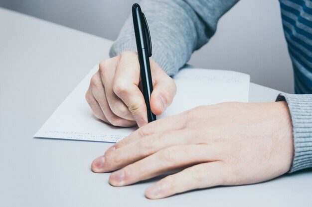 L'uomo si siede al tavolo e scrive con una penna su carta