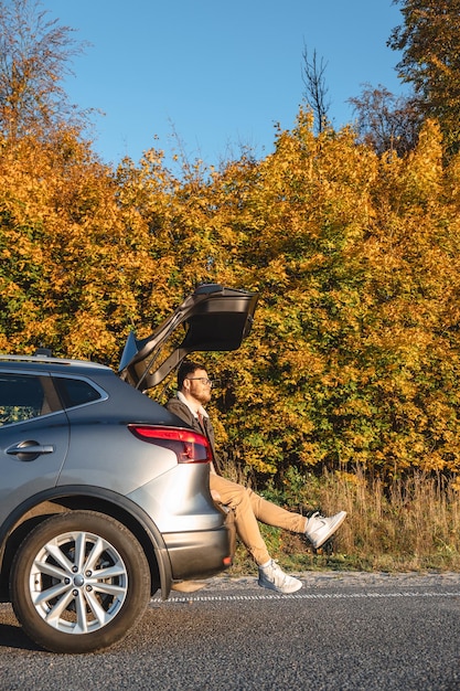 l'uomo si siede nel bagagliaio della sua macchina e si gode il sole d'autunno mentre si crogiola in esso