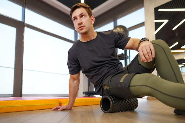 L'uomo si sta massaggiando i muscoli delle gambe con il foam roller