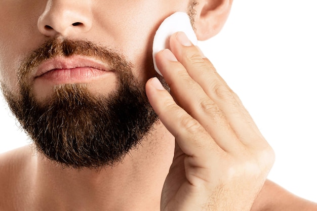 L'uomo si sta pulendo il viso con un batuffolo di cotone su sfondo bianco