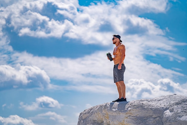 L'uomo si trova su una roccia e beve un frullato di proteine contro il cielo