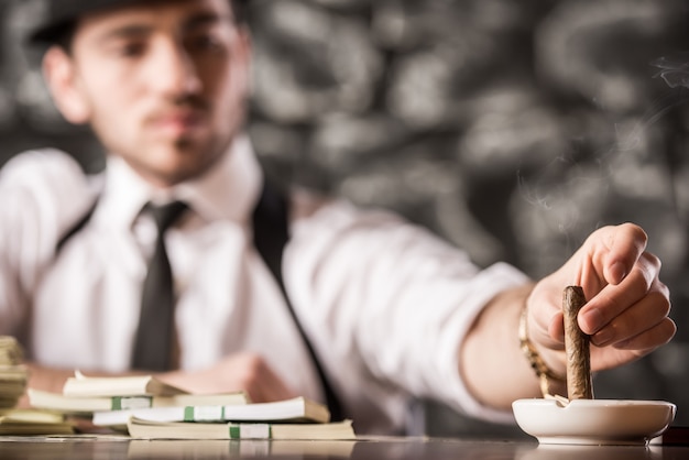 L'uomo sicuro del gangster sta fumando un sigaro cubano.