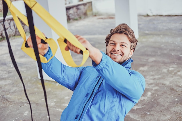 L'uomo sorridente allegro sta facendo esercizi all'esterno usando bende speciali.