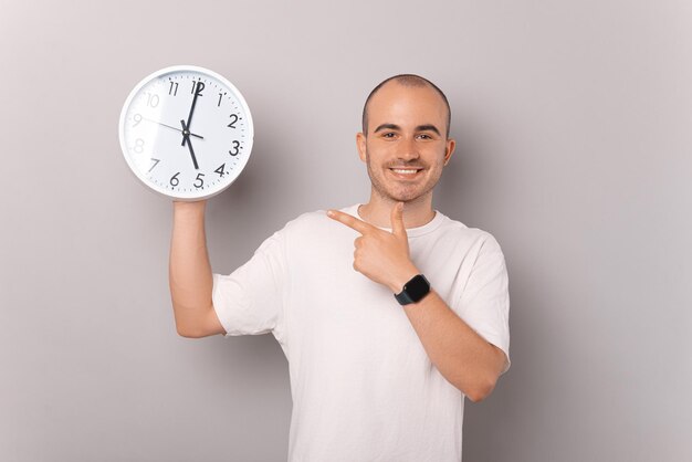 L'uomo sorridente calvo sta indicando l'orologio rotondo bianco che sta tenendo