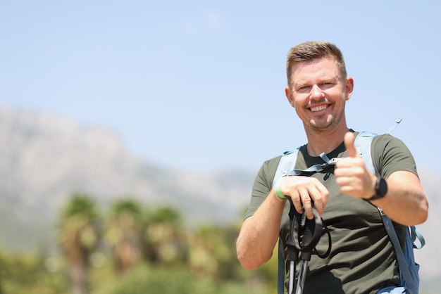 L'uomo sorridente che tiene i pollici in su tiene i bastoncini scandinavi e si erge sui benefici della montagna